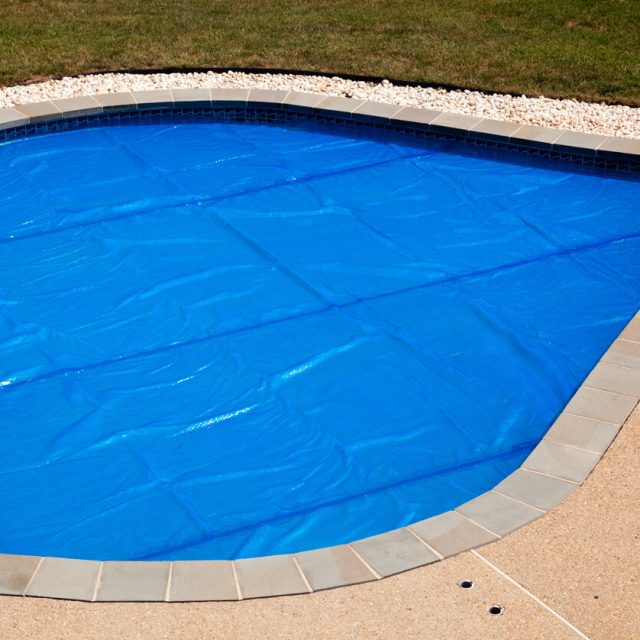 Solar pool cover protecting a backyard swimming pool and retaining heat