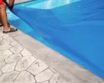 Thumnbail of Person covering swimming pool with a blue solar pool cover for protection